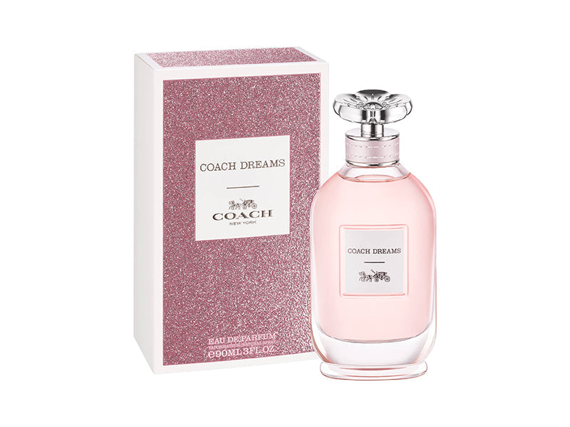 A pink bottle of Coach Dreams 3.4 Edp L with a silver cap, alongside its white box packaging with the Coach brand and product name visible.